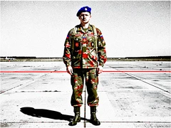 A soldier in full Russian airborne forces uniform stands at attention on a military airfield tarmac, wearing a blue beret and camouflage jacket with insignia patches, parachute harness visible over the shoulders, boots polished, posture rigid and proud. Flat harsh overhead daylight bleaches the concrete surface, casting hard short shadows beneath the figure. Raw photocopy zine aesthetic, brutalist DIY print energy with high-contrast pure white #FFFFFF and pure black #000000, disrupted by aggressive red #FF0000 accents and muted grey #F2F2F2 mid-tones. Flat hard daylight with crushed shadows and no soft falloff. Style: brutalist zine. Mood: confrontational.
