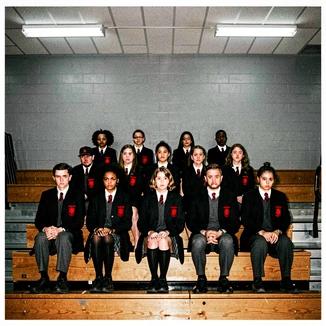 A group photo of twelve people in school uniforms on gymnasium bleachers, with one face in the front row naturally replaced and blended to match the flat fluorescent lighting of the room. Skin tone and shadow direction are consistent with the surrounding faces. The grey wall background is unchanged. Atmosphere is institutional and even. Raw photocopy zine aesthetic, brutalist DIY print energy with high-contrast pure white #FFFFFF and pure black #000000, disrupted by aggressive red #FF0000 accents and muted grey #F2F2F2 mid-tones. Flat hard daylight with crushed shadows and no soft falloff. Style: brutalist zine. Mood: confrontational.
